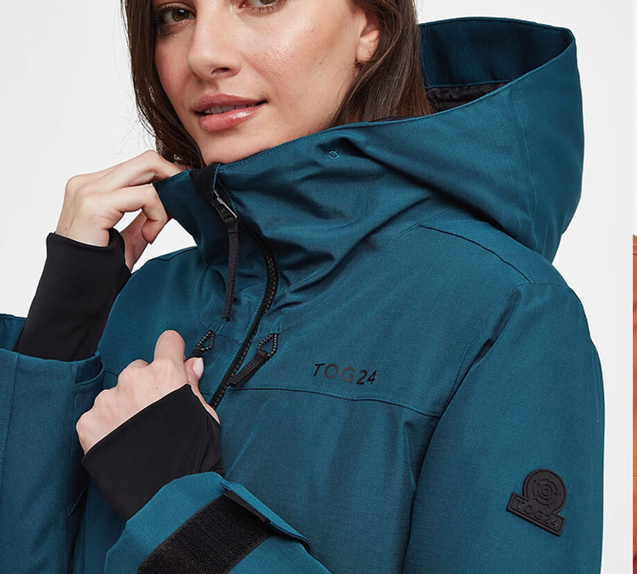 Close-up of a woman wearing a teal TOG24 waterproof jacket with hood and black detailing.