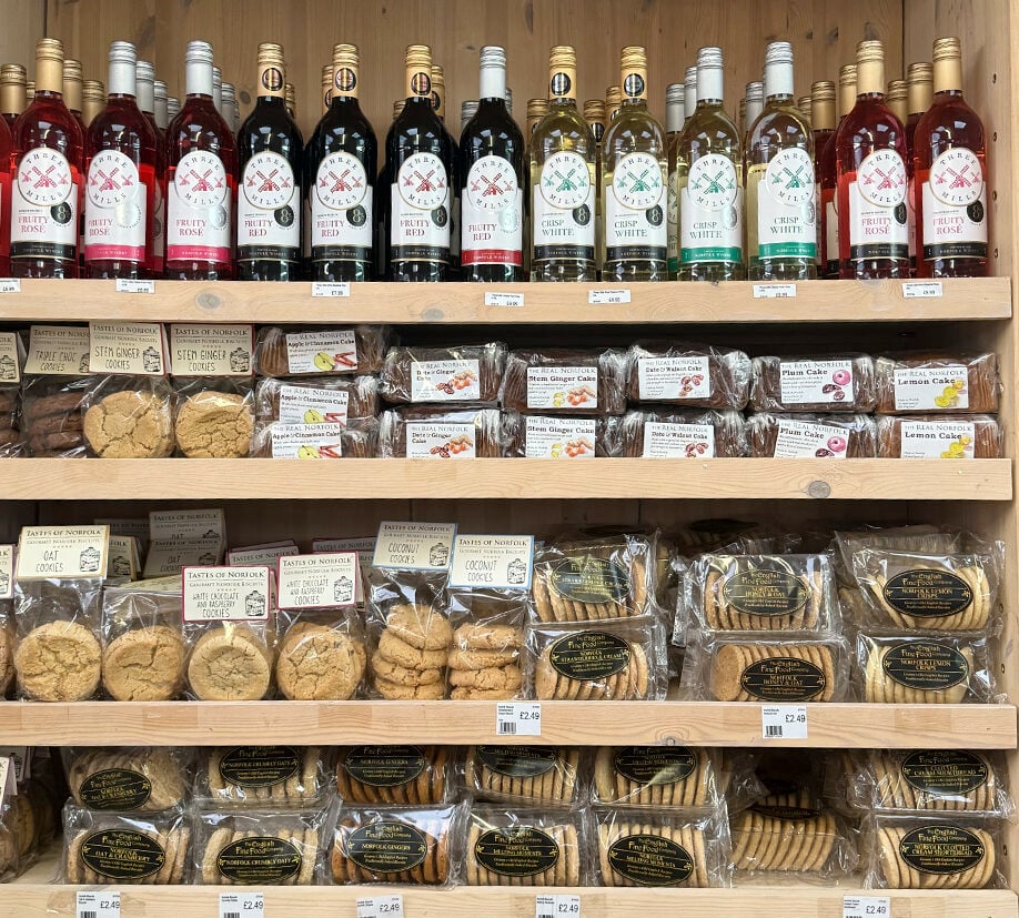 Shelves stocked with bottles of wine and locally made Norfolk cookies, cakes, and biscuits arranged neatly in a shop display.