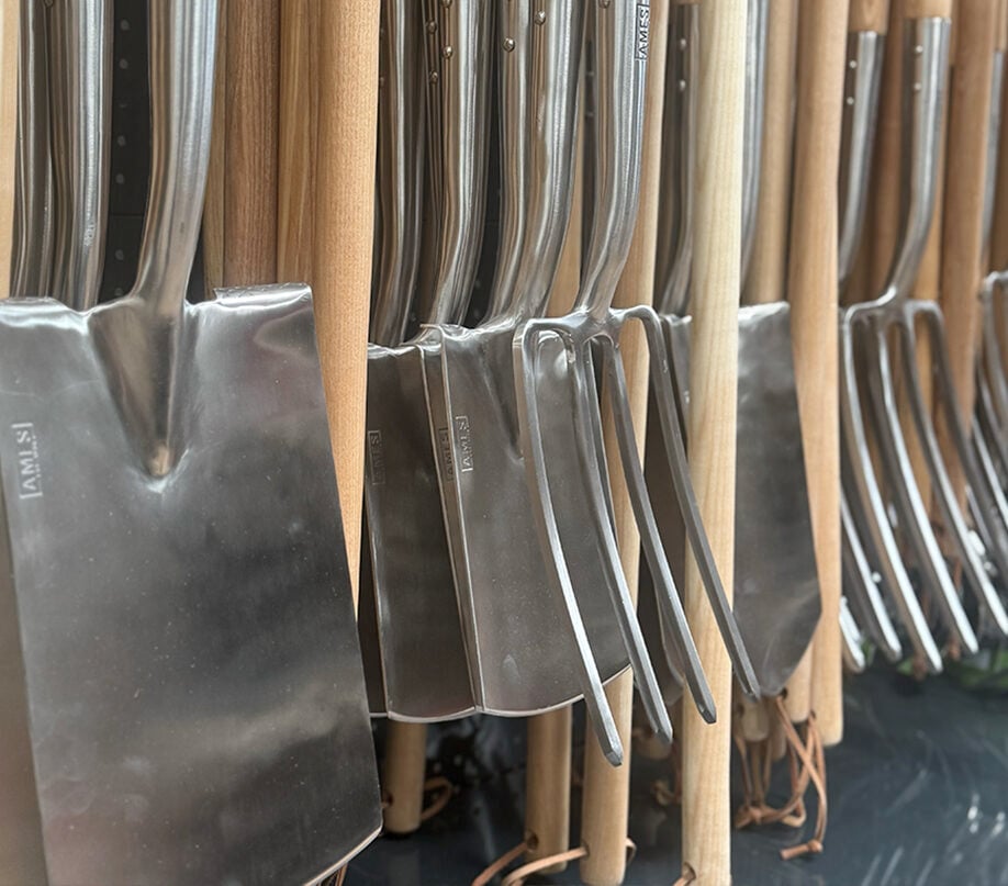 Close-up of stainless steel garden spades and forks with wooden handles neatly arranged on display.