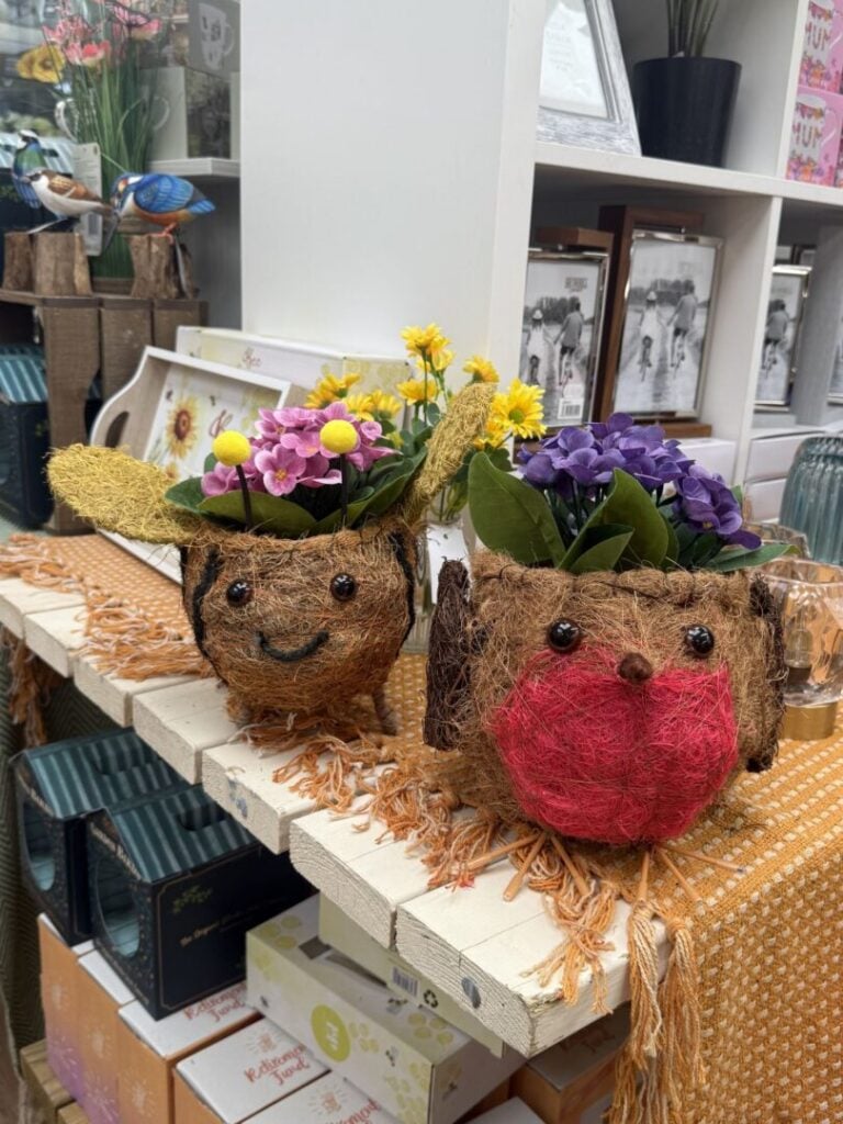 Two decorative animal-shaped planters made from natural fibres, filled with colourful artificial flowers on a shop display.
